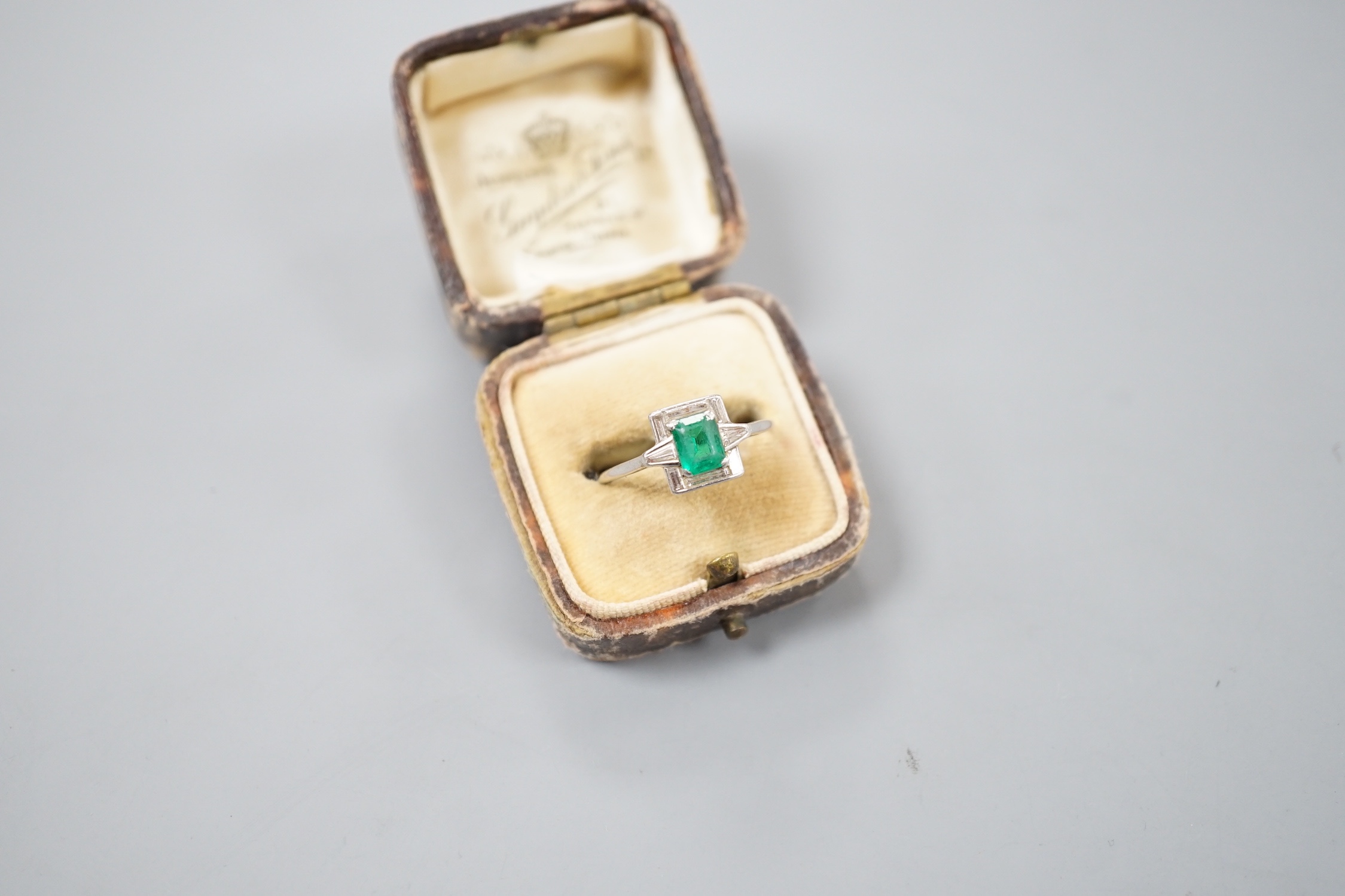 An Art Deco white metal, single stone emerald, baguette and trapeze cut diamond cluster set ring, size R/S, gross 3.5 grams
